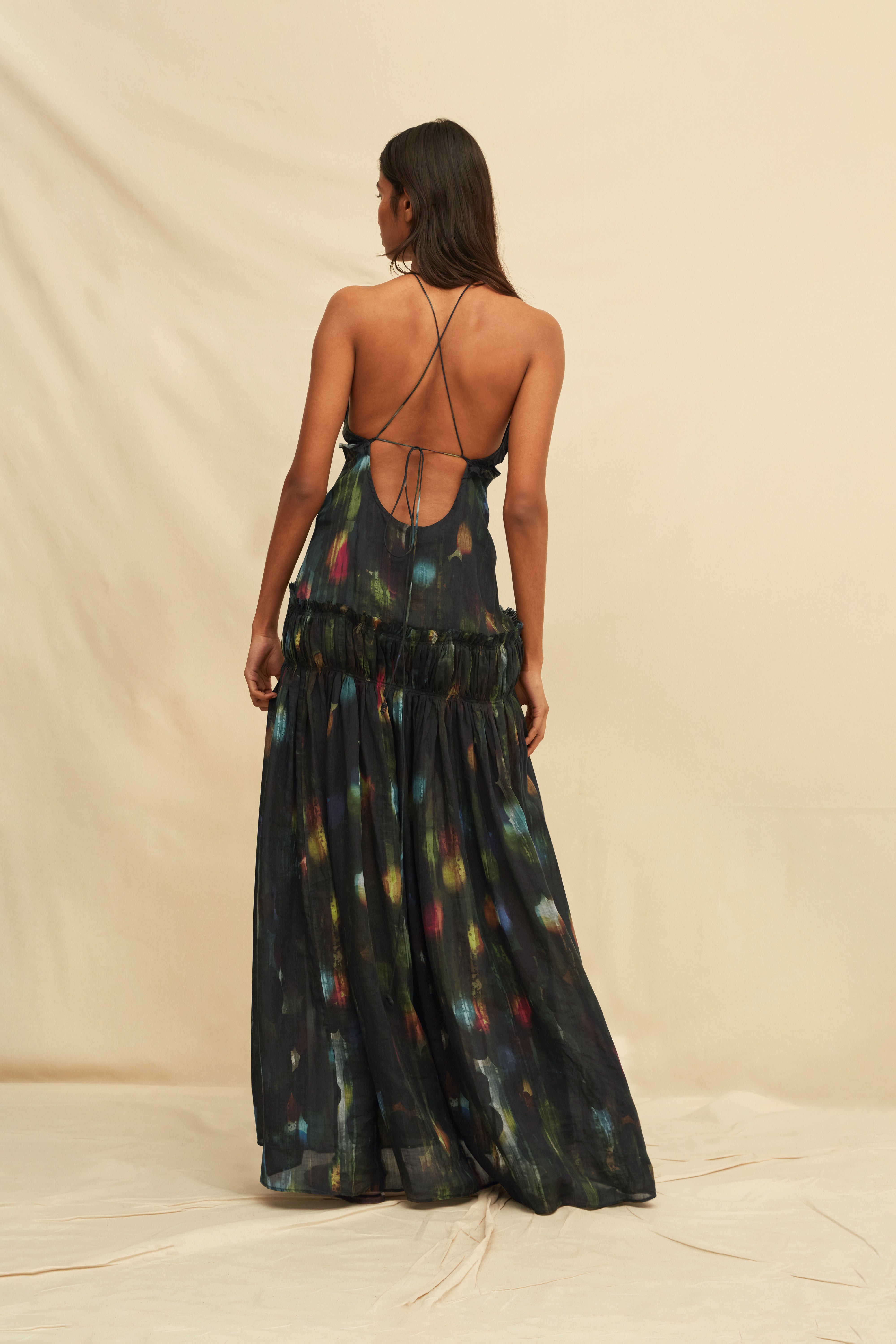 Woman wearing a long, dark painterly printed dress with a backless design, on a beige background