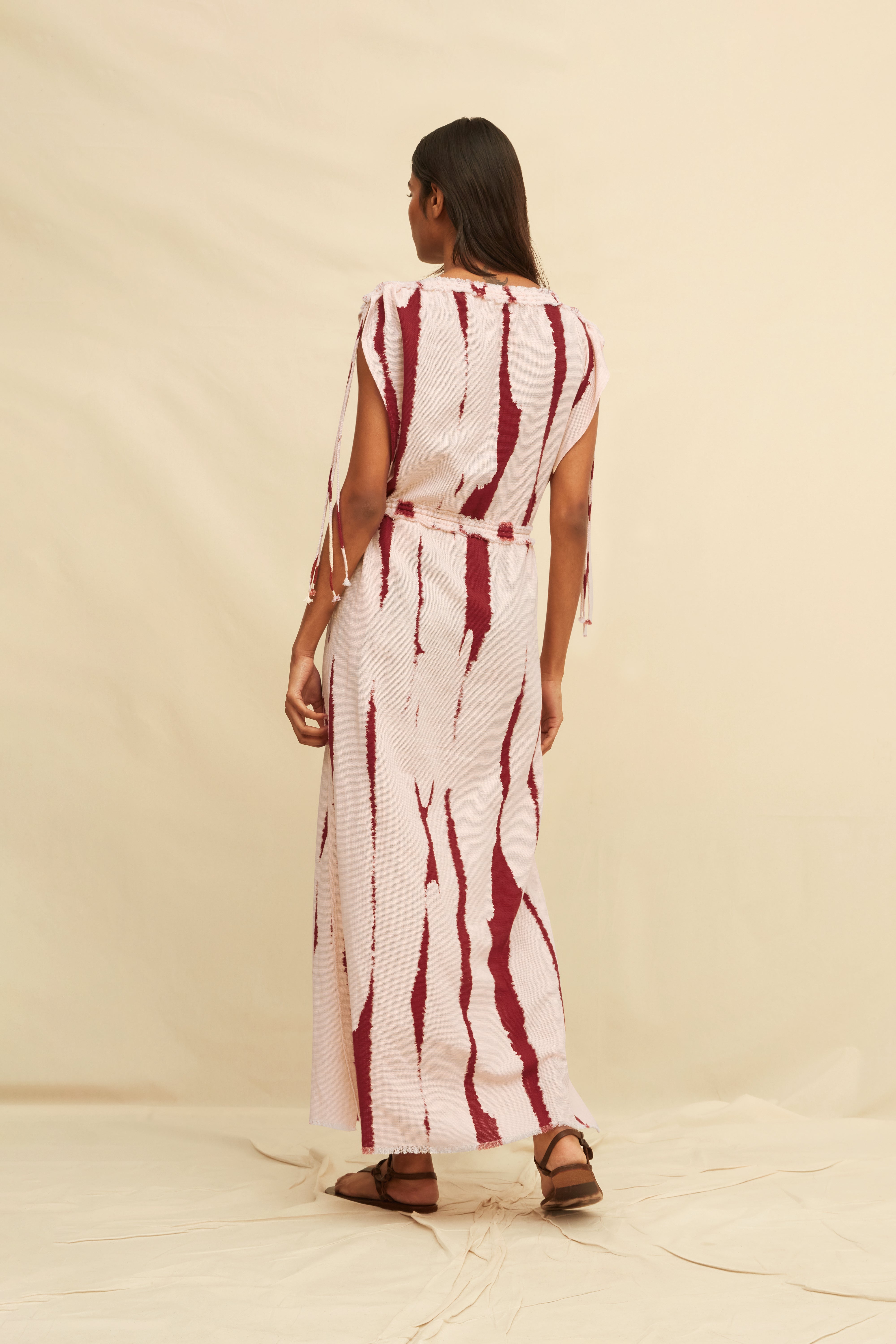 Woman wearing a long tie-dye sheath dress holding on a beige background