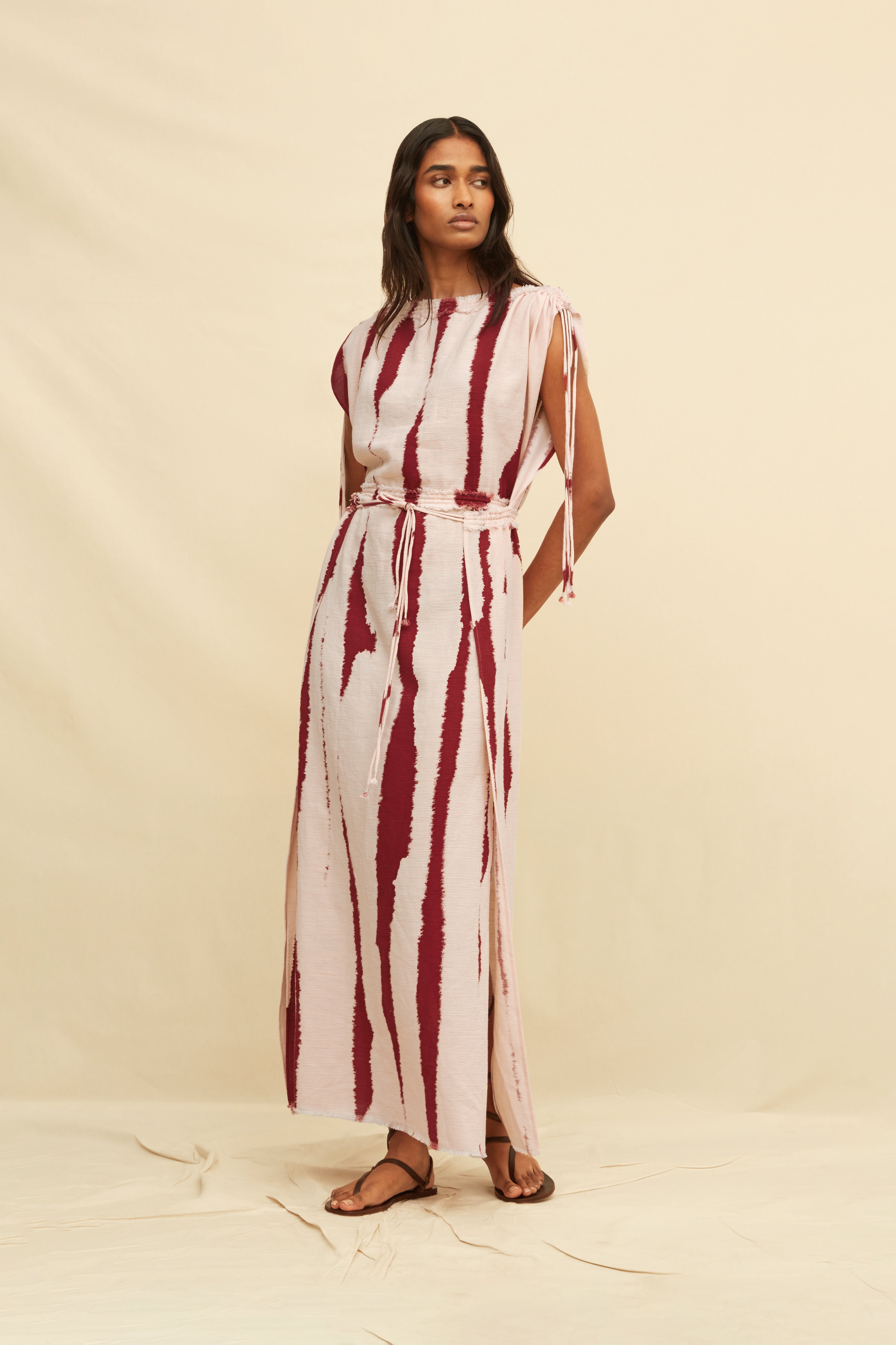 Woman wearing a long tie-dye sheath dress holding on a beige background