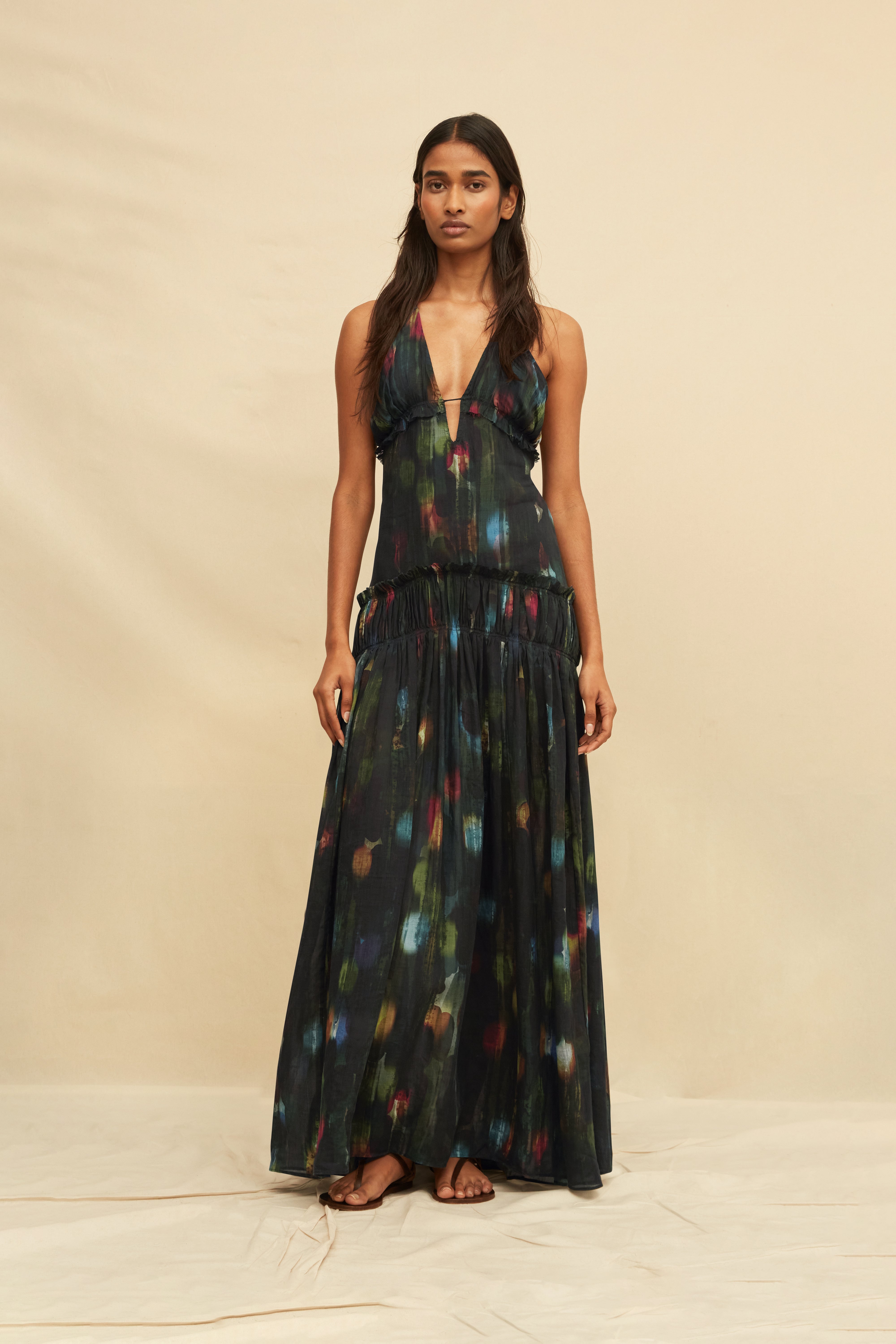 Woman wearing a long, dark-colored dress with colorful abstract patterns on a beige background