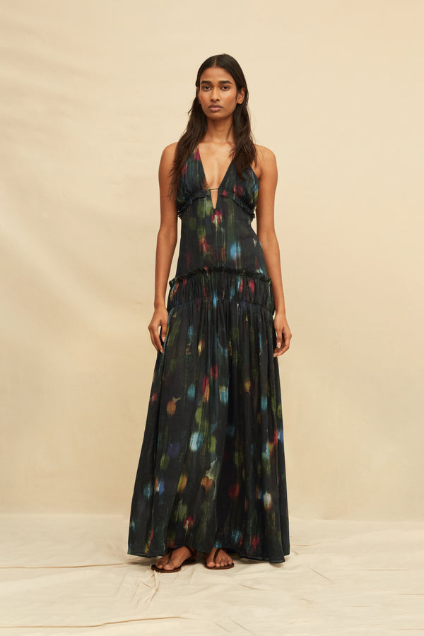 Woman wearing a long, dark-colored dress with colorful abstract patterns on a beige background