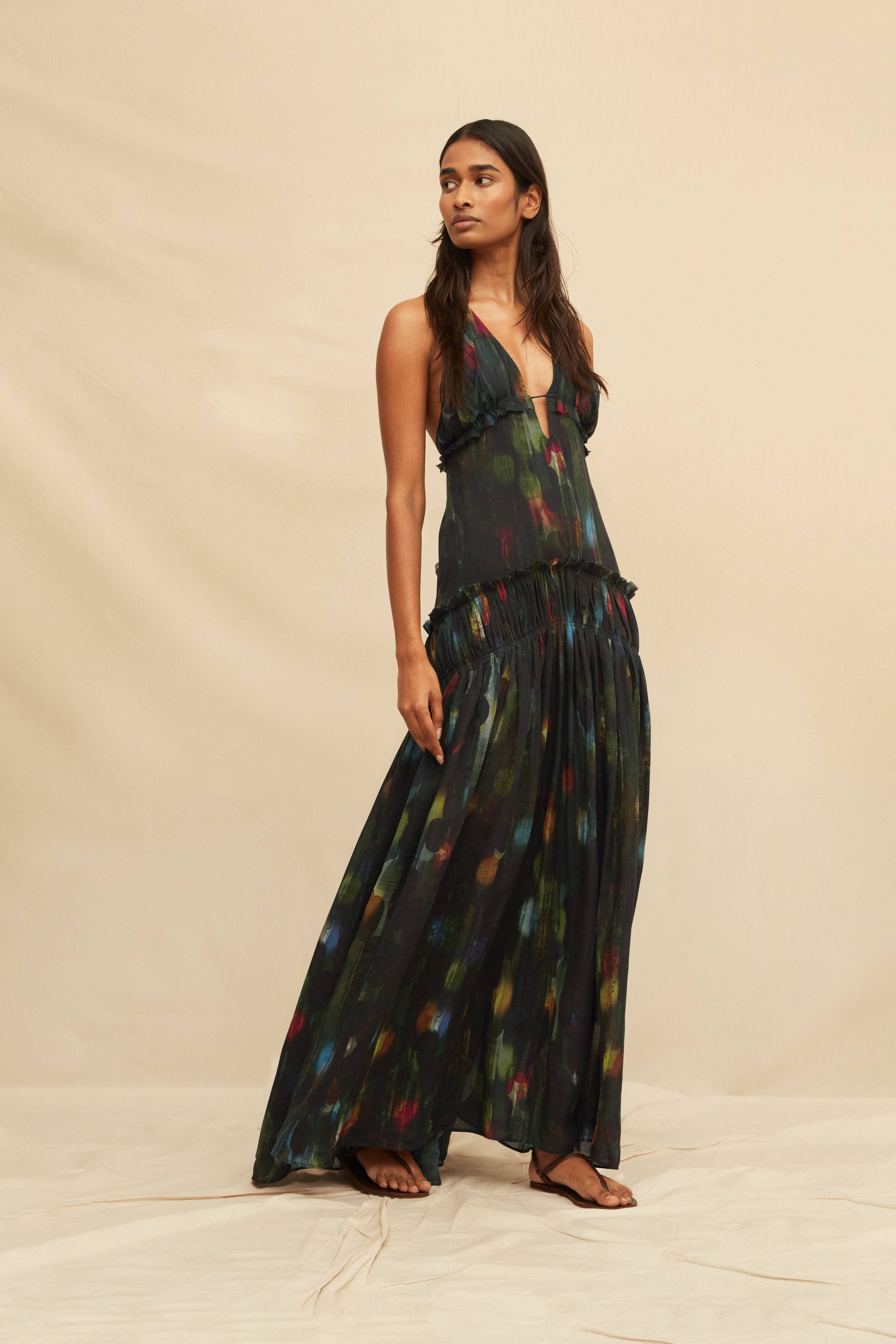Woman wearing a long, dark green dress with colorful abstract patterns on a beige background