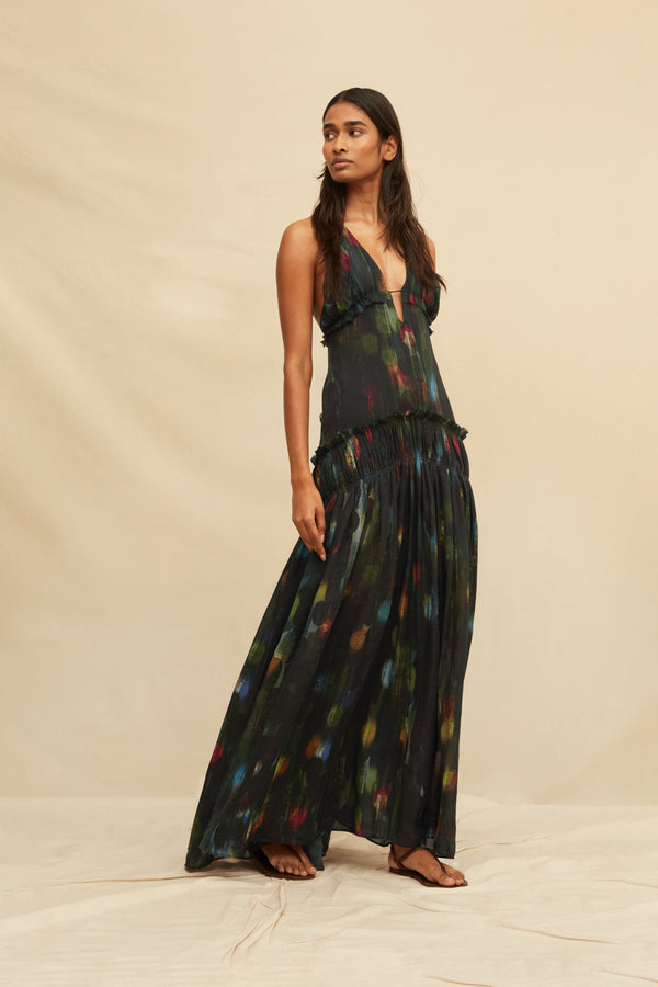Woman wearing a long, dark green dress with colorful abstract patterns on a beige background