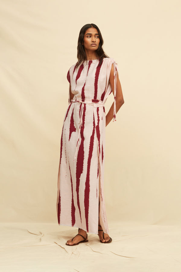 Woman wearing a long tie-dye sheath dress holding on a beige background