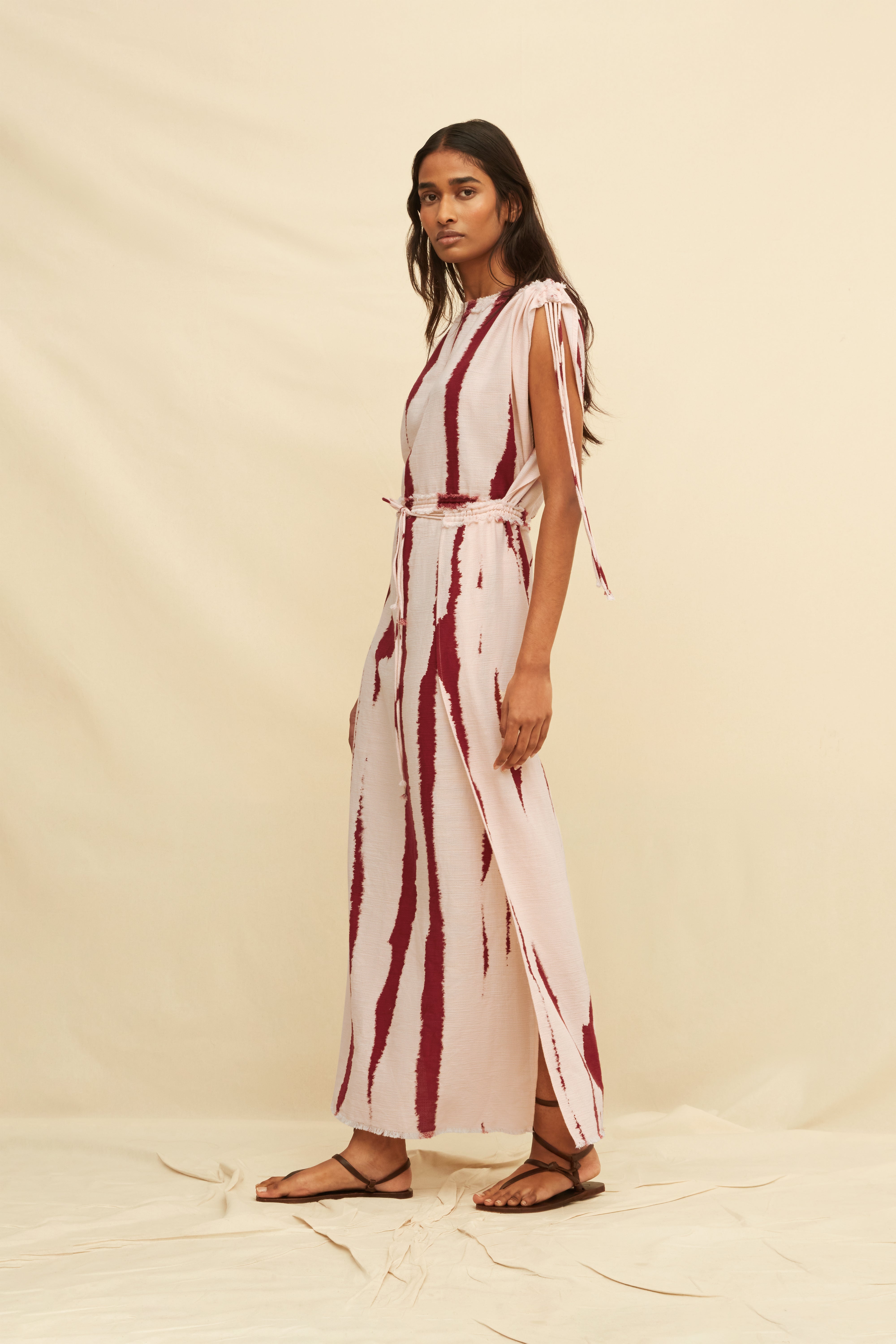 Woman wearing a long tie-dye sheath dress holding on a beige background