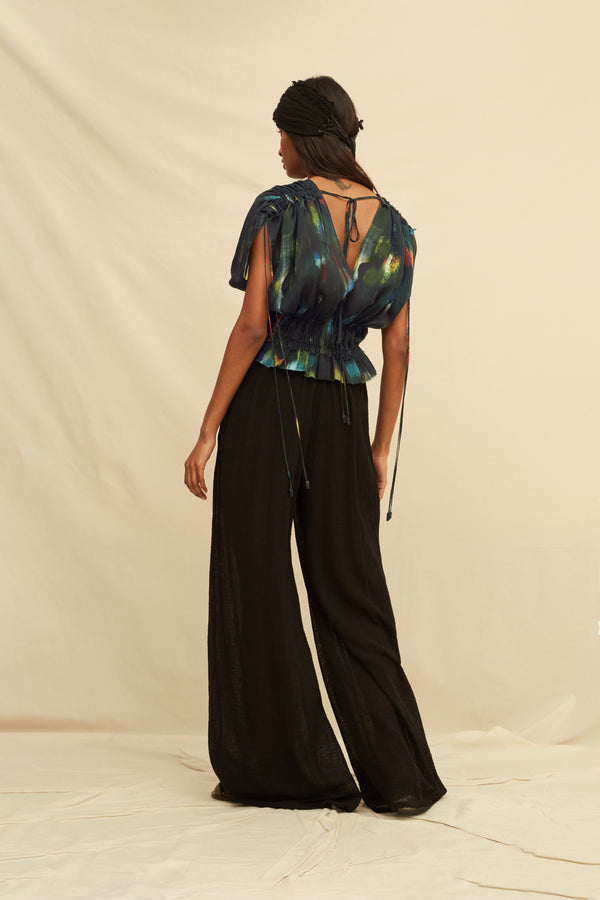 Woman wearing a black blouse with abstract painterly pattern, paired with black trousers and a black turban, on a beige background