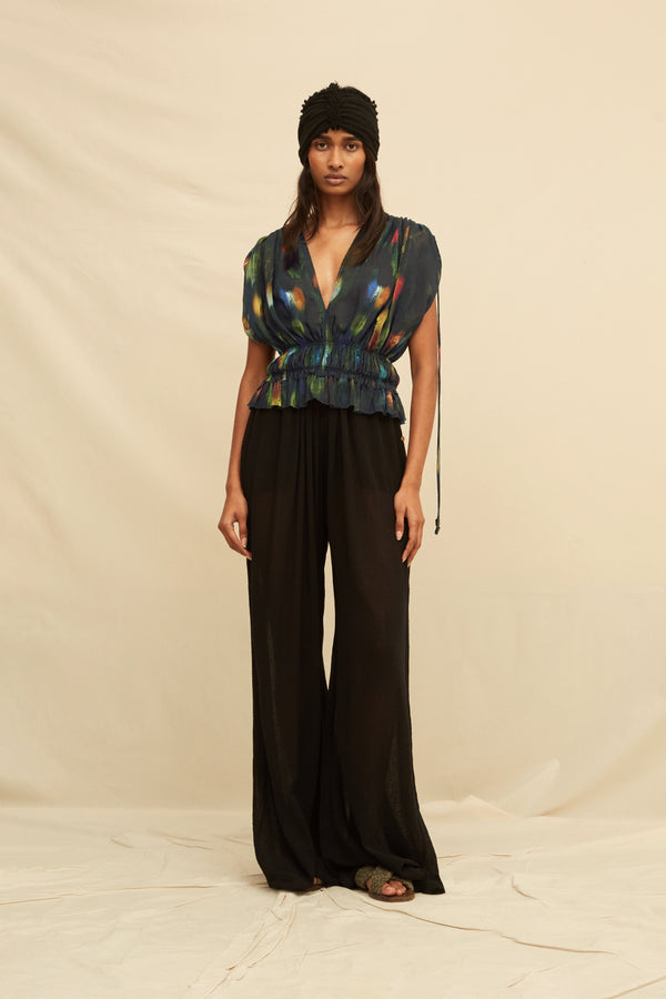 Woman wearing a black blouse with abstract painterly pattern, paired with black trousers and a black turban, on a beige background