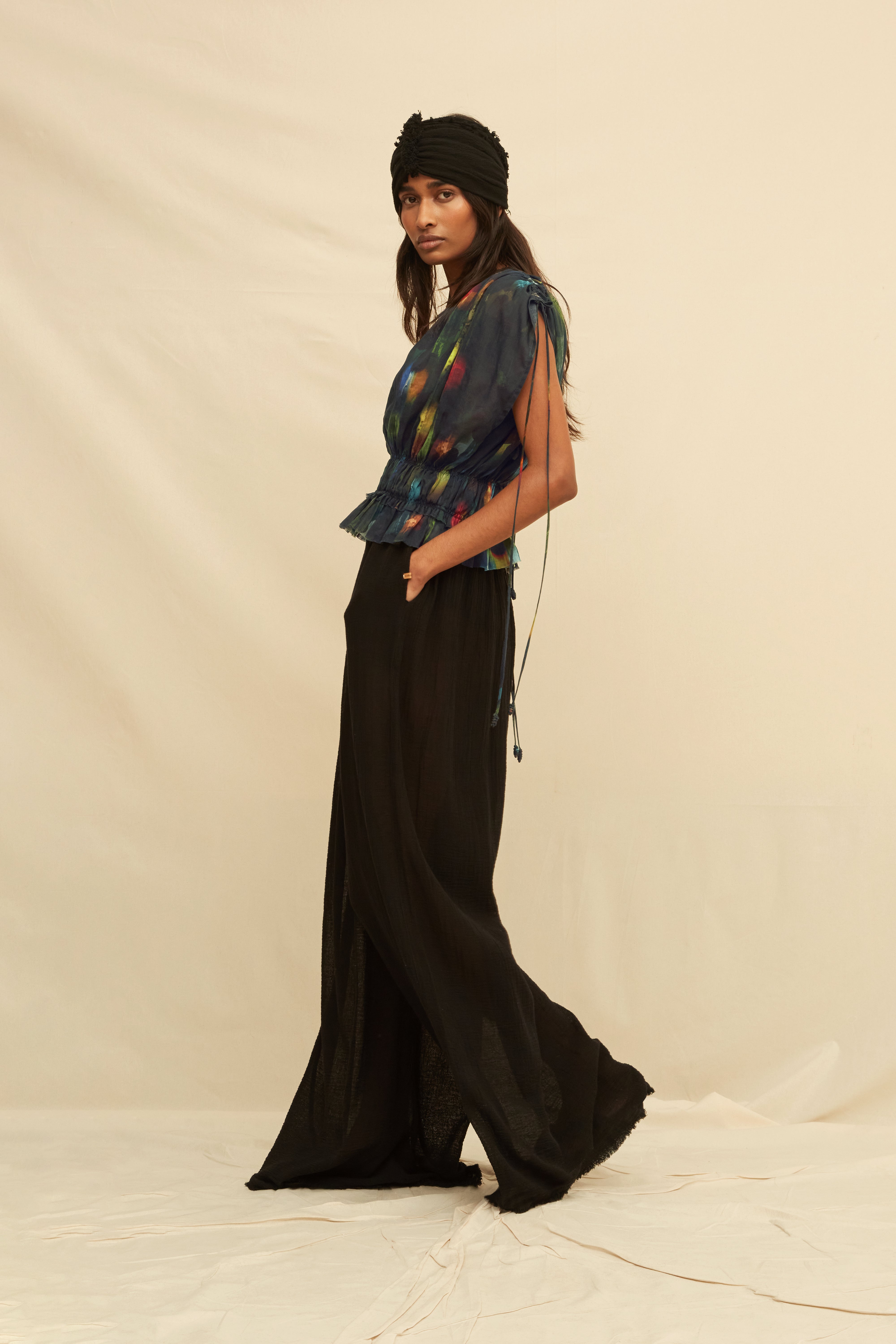 Woman wearing a black blouse with abstract painterly pattern, paired with black trousers and a black turban, on a beige background
