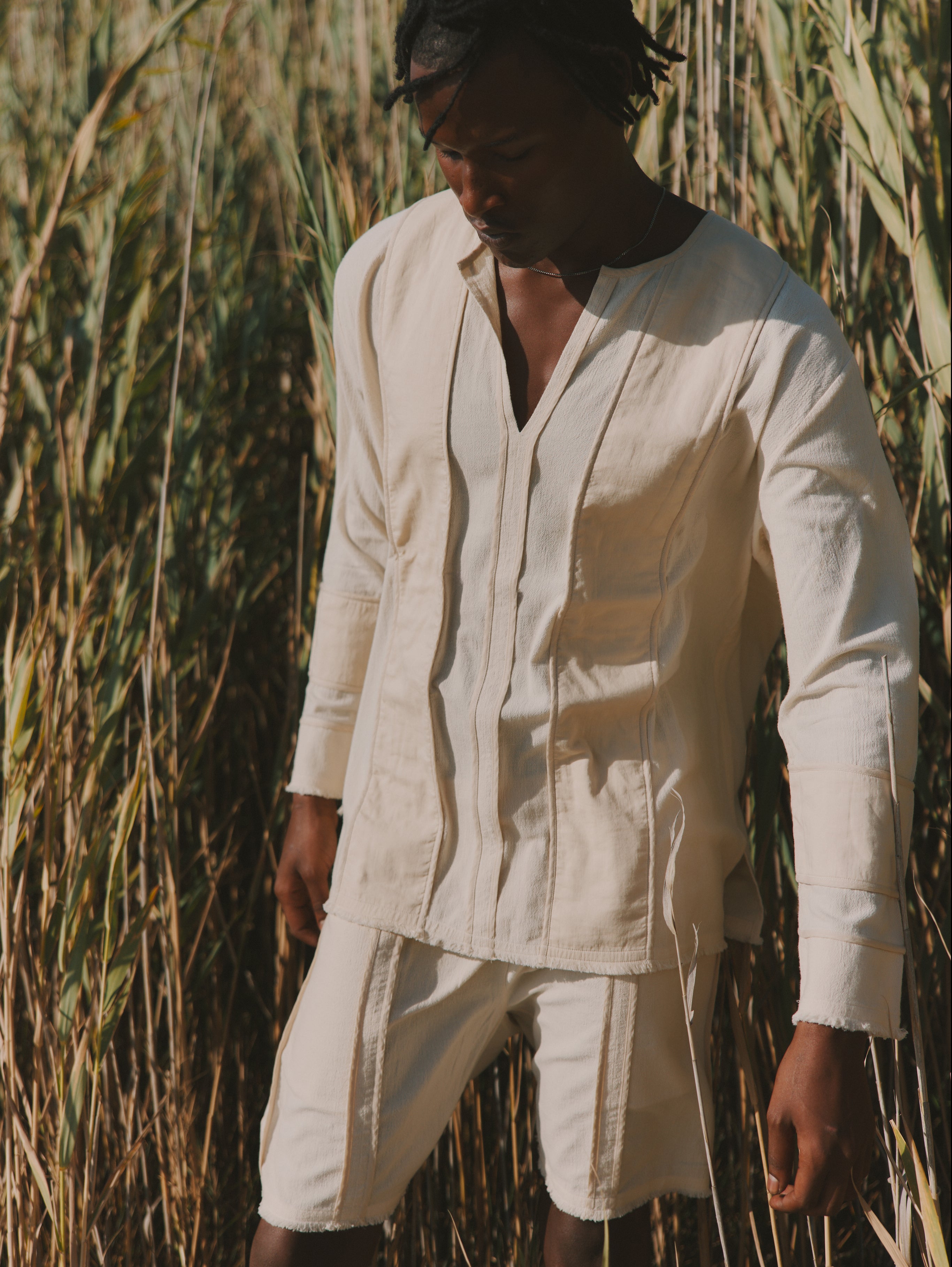 Man wearing a light-colored shirt and pants standing in tall grass.