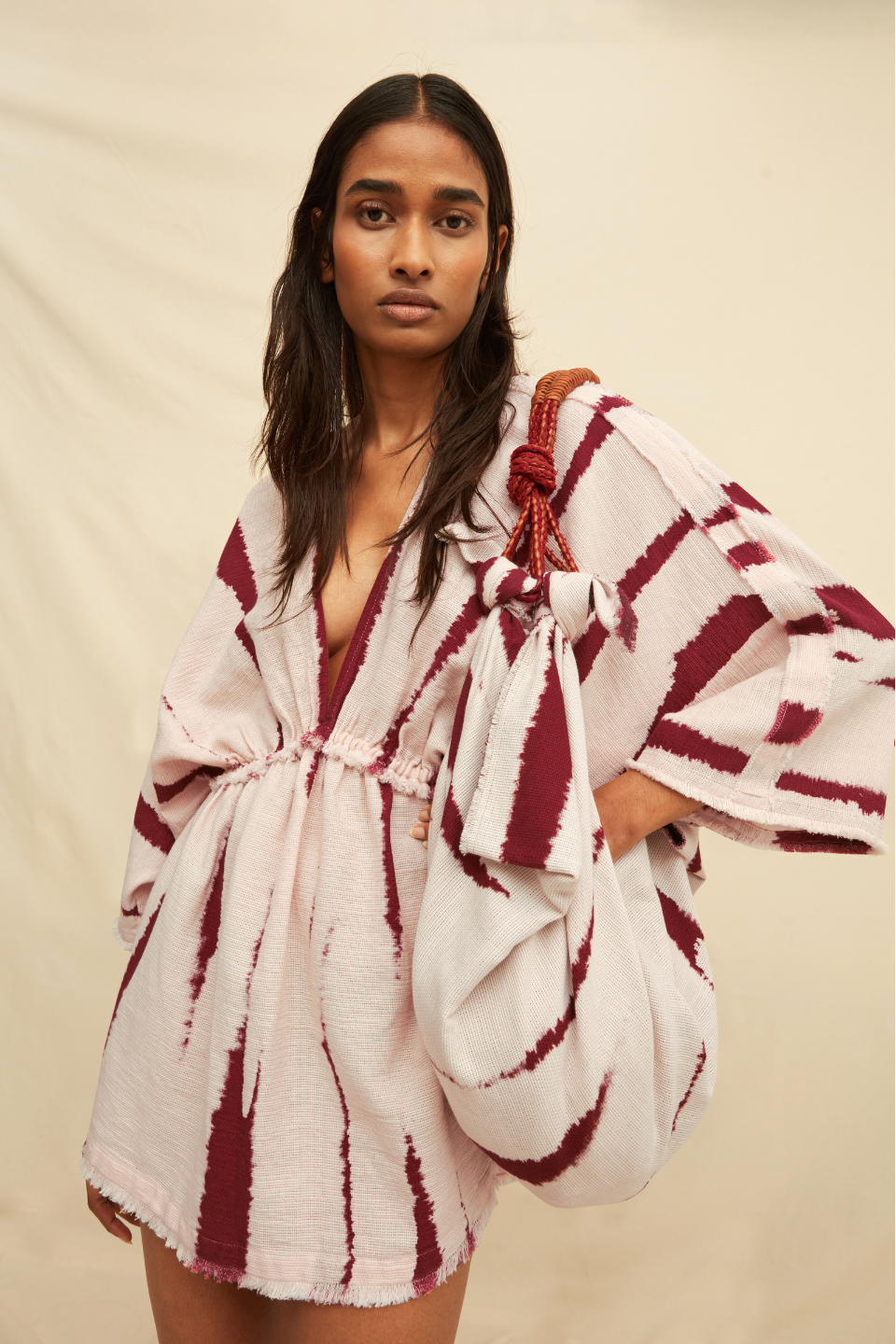 Woman wearing a tie-dye kaftan dress holding a matching bag on a beige background