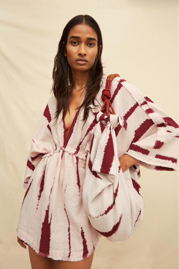 Woman wearing a tie-dye kaftan dress holding a matching bag on a beige background