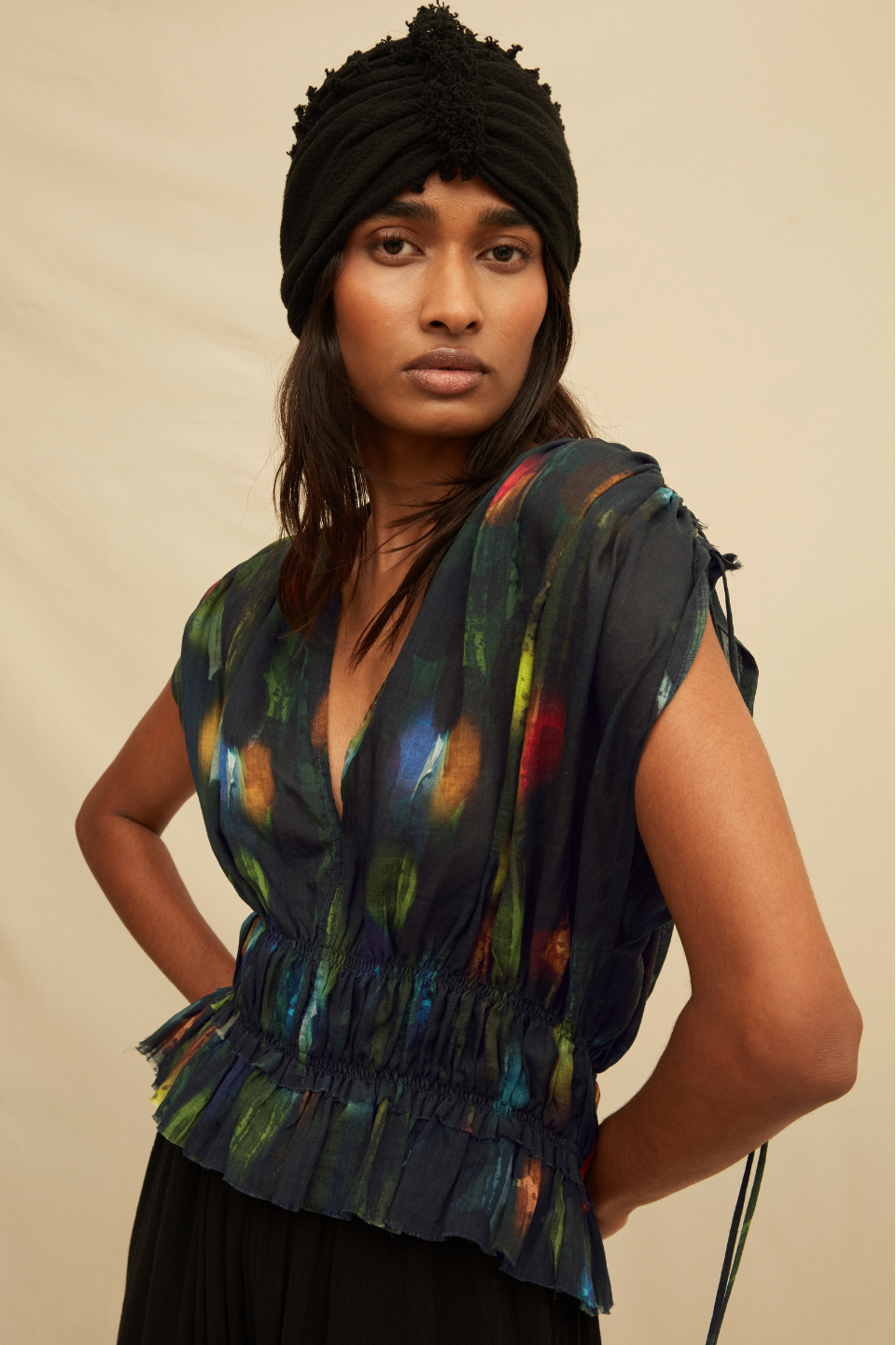 Woman wearing a black blouse with abstract painterly pattern and a black turban, on a beige background